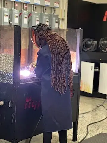 A person with long hair welding in an industrial setting.